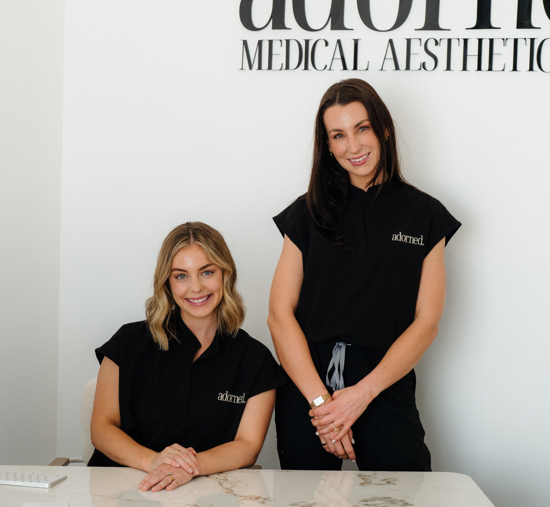 Two women in black shirts with 'adorned' logo standing in front of a Medical Aesthetics' sign.